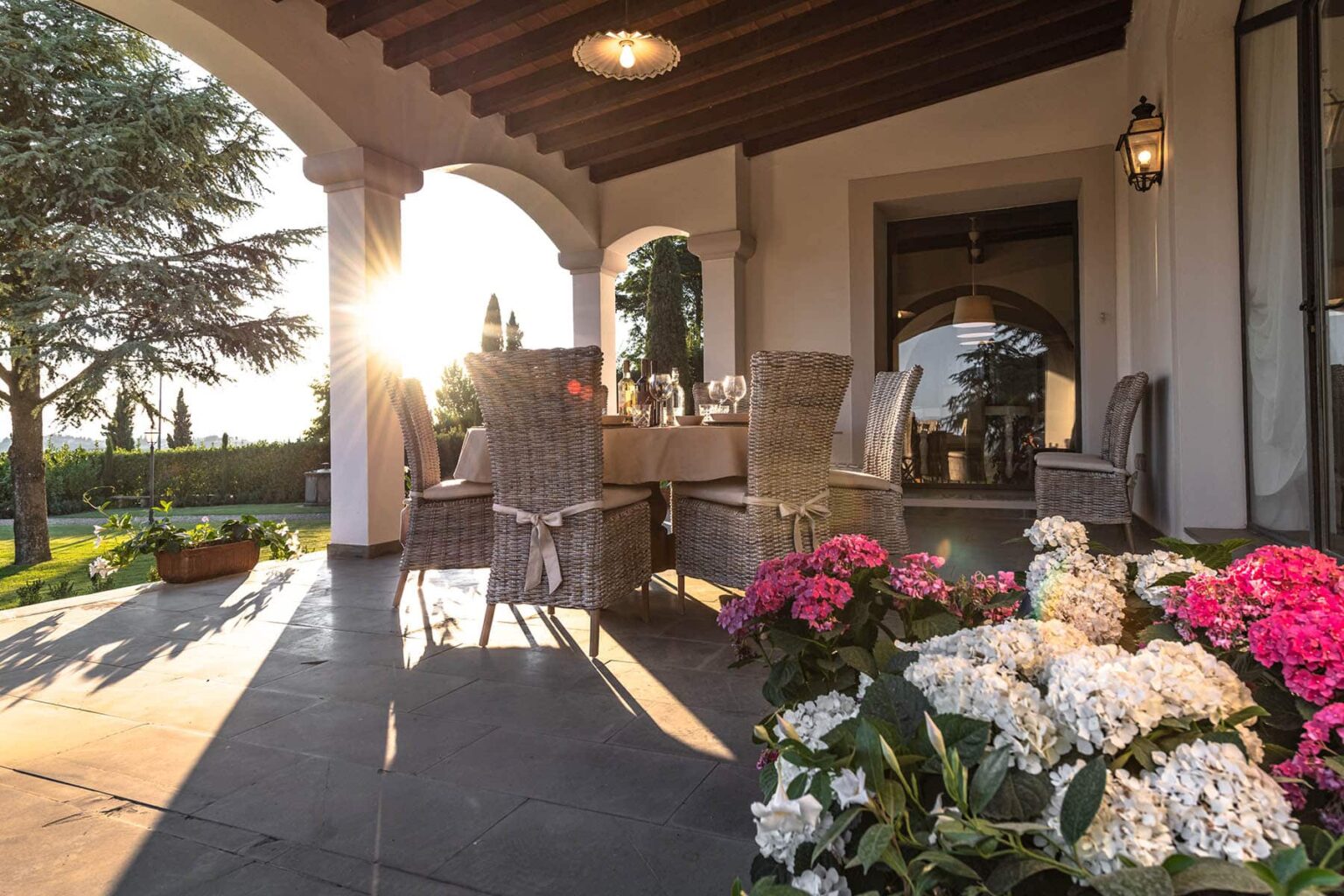 Cozy outdoor patio with wicker furniture and blooming flowers, illuminated by warm sunset light, creating a serene atmosphere for relaxation. | Only on SopranoVillas