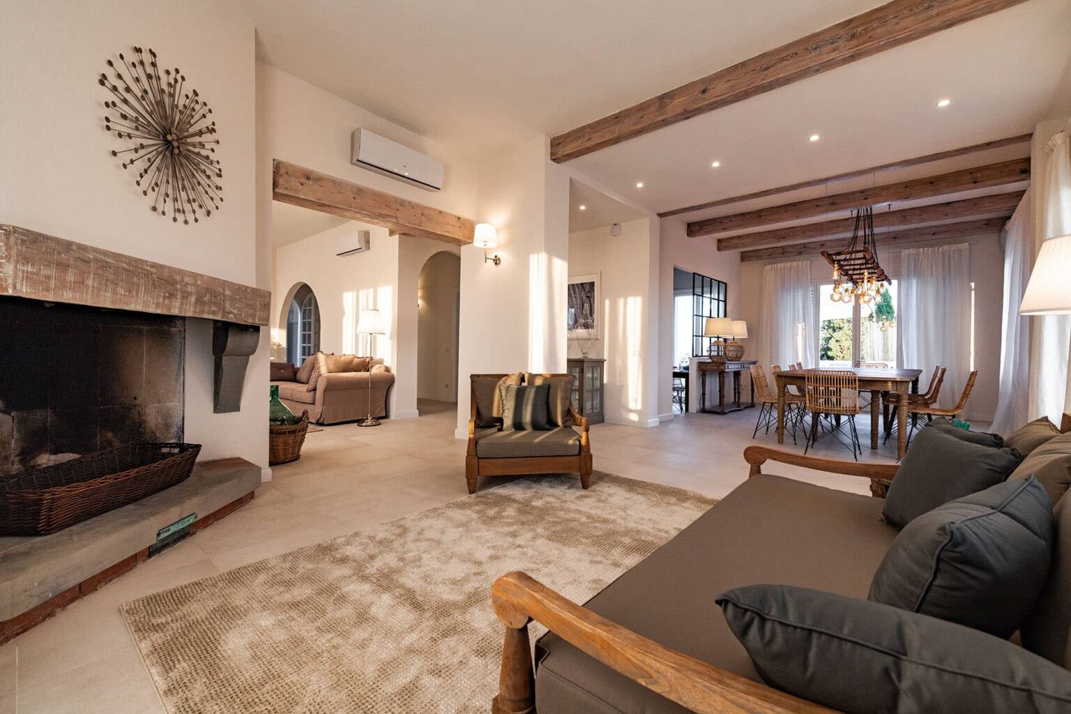 Modern living room with wooden beams, a cozy fireplace, and stylish furniture, featuring a comfortable sofa and a dining area with natural light. | Only on SopranoVillas