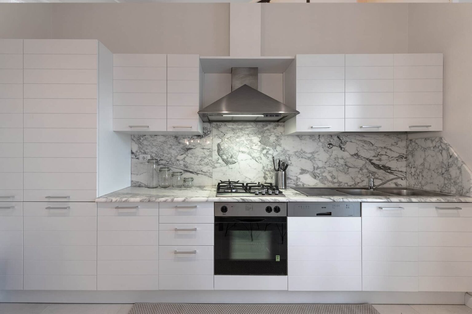 Modern kitchen design featuring white cabinetry, a sleek marble backsplash, stainless steel appliances, and a contemporary range hood. Ideal for showcasing minimalist and elegant home interiors. | Only on SopranoVillas