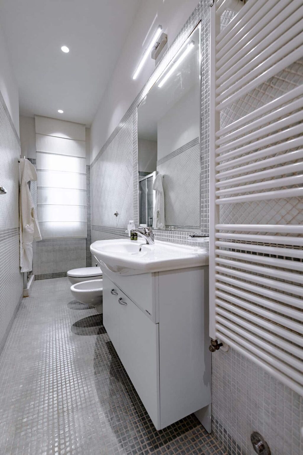 Modern bathroom interior featuring a white sink, toilet, and heated towel rack, with sleek tile walls and ample natural light. | Only on SopranoVillas
