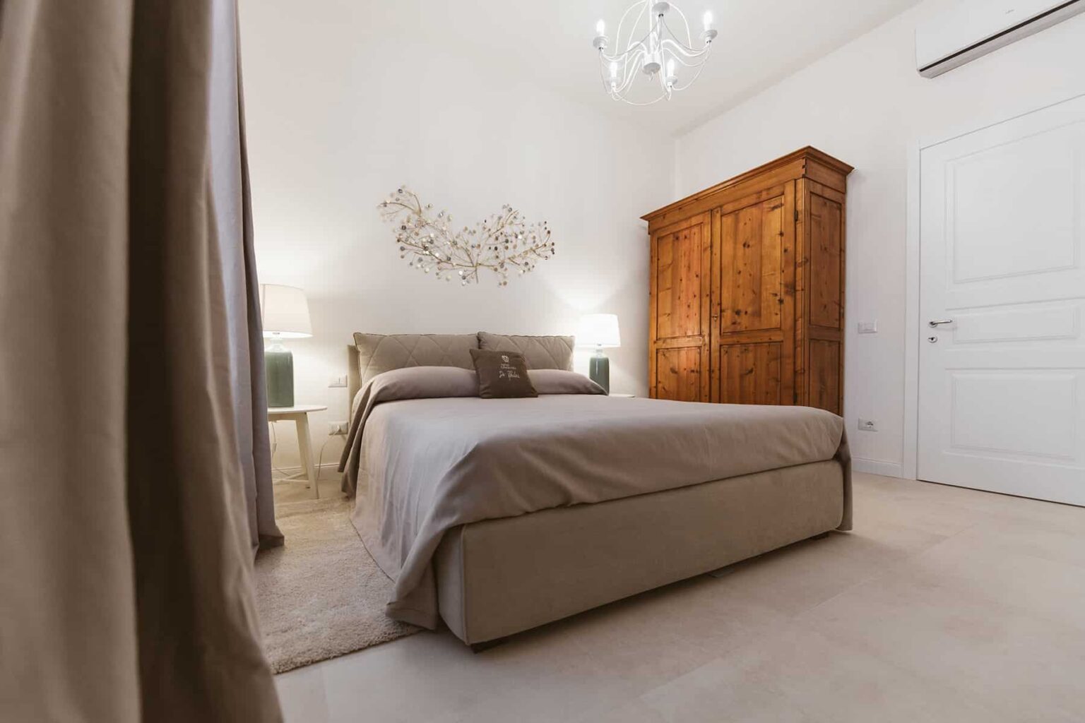 Cozy bedroom featuring a beige bed with elegant bedding, a wooden wardrobe, soft lighting, and neutral decor, creating a warm and inviting atmosphere. | Only on SopranoVillas