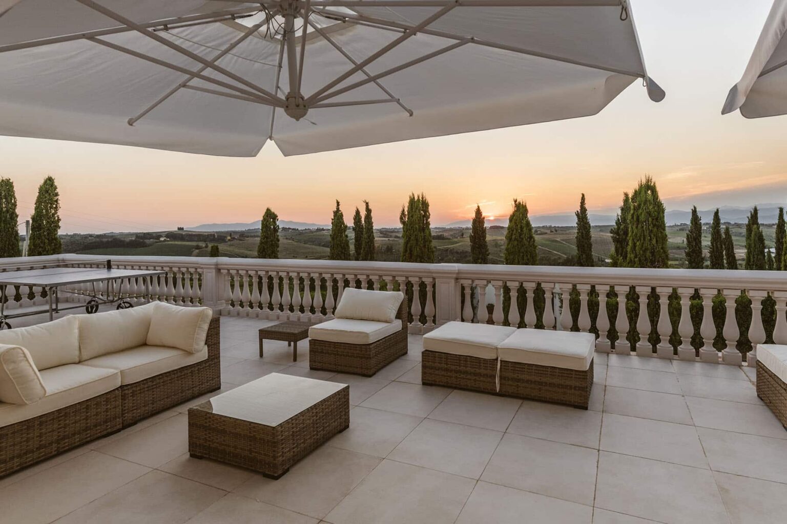 Outdoor terrace with stylish furniture, including a seating area and coffee table, overlooking a scenic sunset and lush greenery. Ideal for relaxation and entertaining. | Only on SopranoVillas