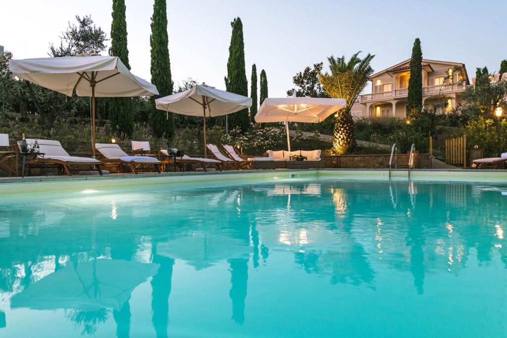 Luxurious outdoor swimming pool surrounded by sun loungers and umbrellas, with a scenic villa and lush greenery in the background, perfect for relaxation and leisure. | Only on SopranoVillas