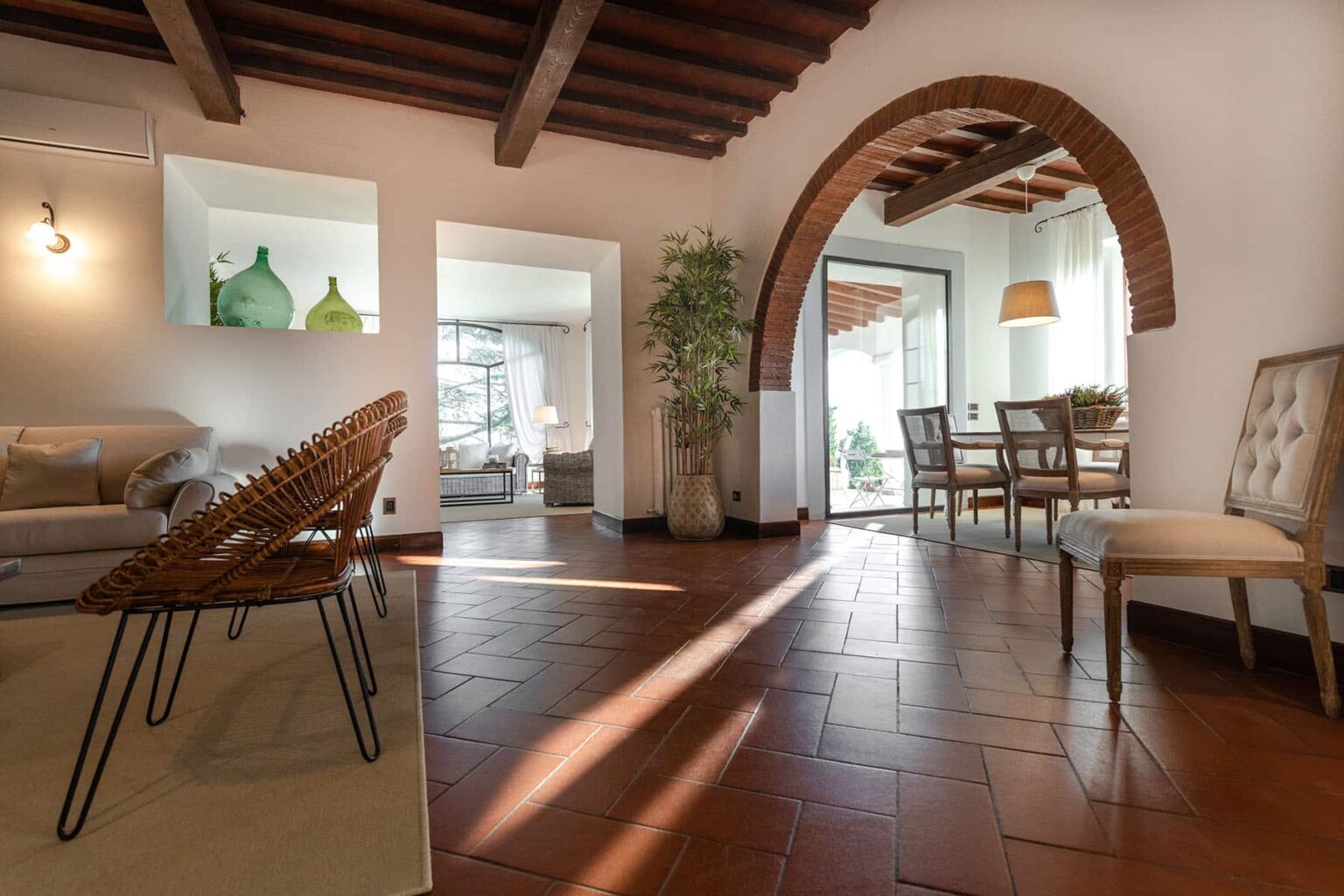 Spacious living area featuring rustic wooden beams, terracotta flooring, and an elegant archway leading to a dining space. Natural light streams in, highlighting stylish furniture and decorative plants. | Only on SopranoVillas