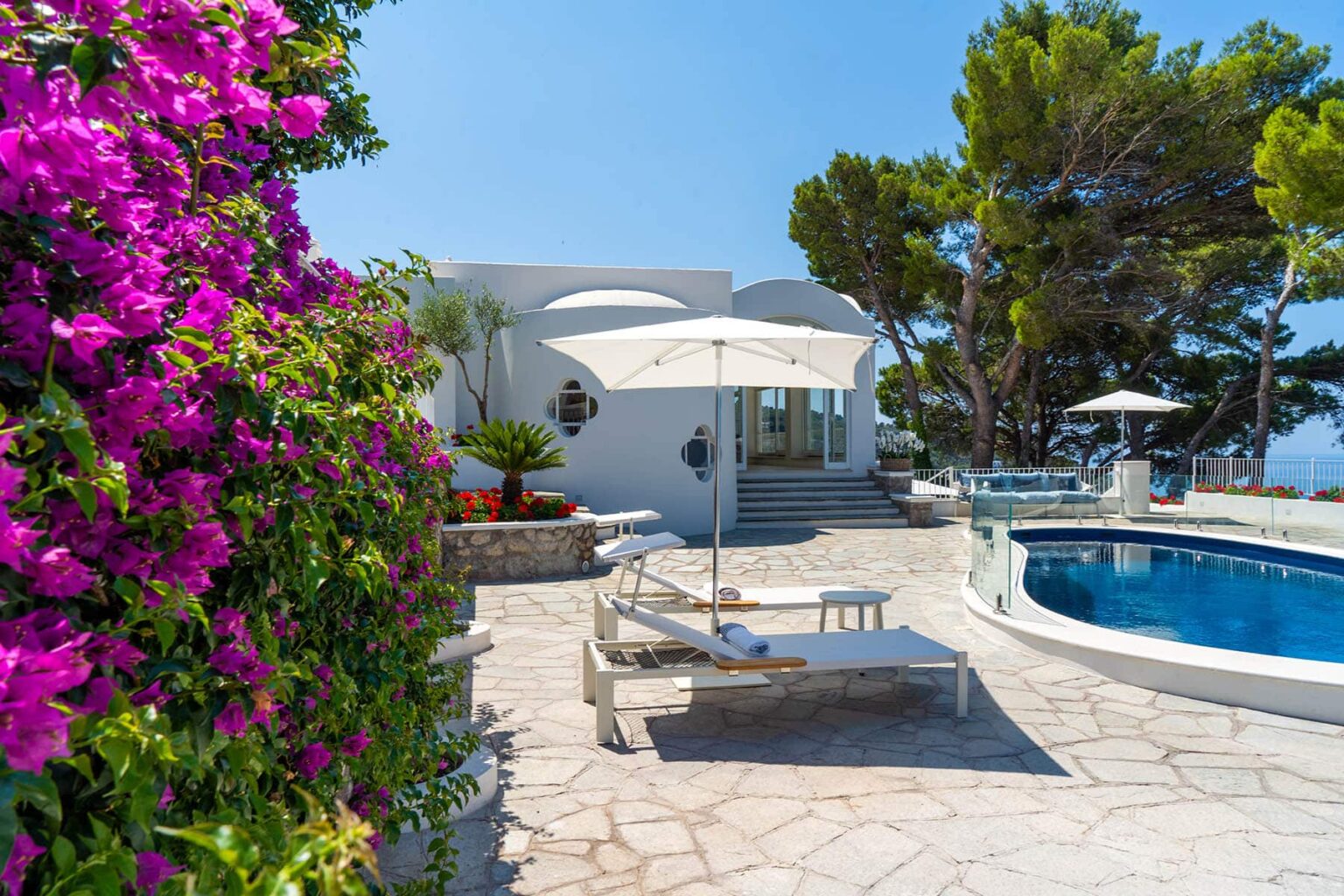 Luxurious villa with a pool surrounded by vibrant bougainvillea flowers and sunny patio, ideal for relaxation in a Mediterranean setting. | Only on SopranoVillas