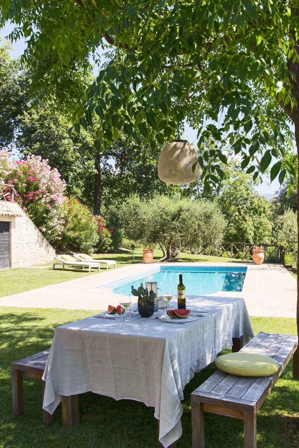 Serene outdoor poolside setting with a table featuring wine and snacks, surrounded by lush greenery and flowering plants, perfect for relaxation and outdoor entertaining. | Only on SopranoVillas
