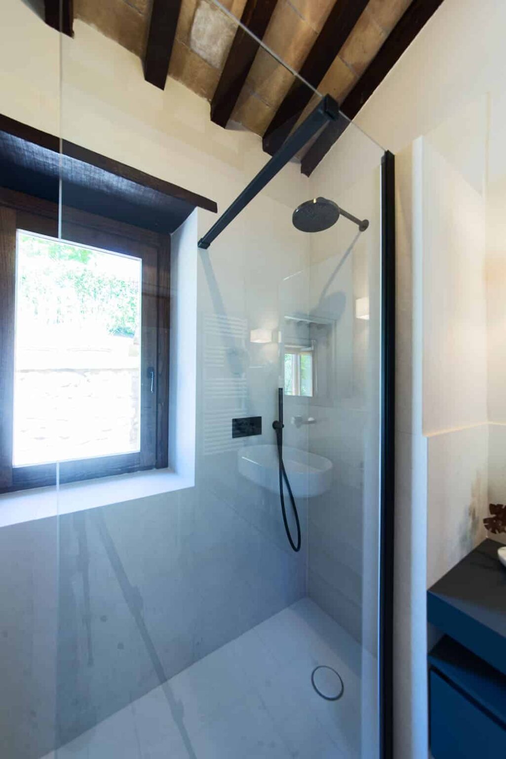Modern glass shower enclosure with a rainfall showerhead, featuring a sleek design and natural light from a nearby window in a contemporary bathroom setting. | Only on SopranoVillas