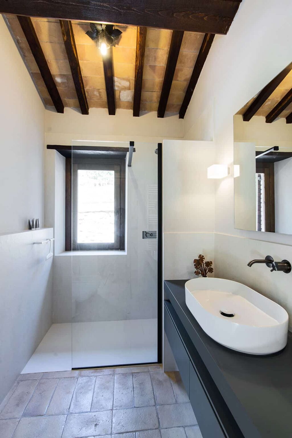 Modern bathroom interior featuring a sleek shower, oval sink, and natural light from a window, complemented by minimalist decor and a contemporary mirror. | Only on SopranoVillas