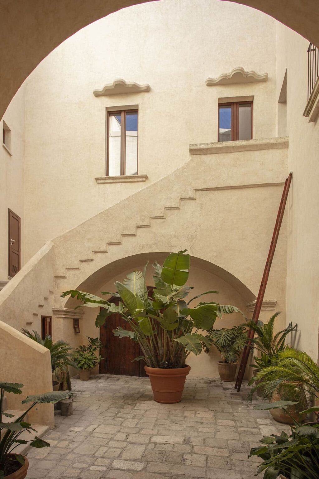 Interior view of a stylish staircase in a modern architectural space, featuring a potted plant at the base and natural light filtering through large windows, creating an inviting atmosphere. | Only on SopranoVillas