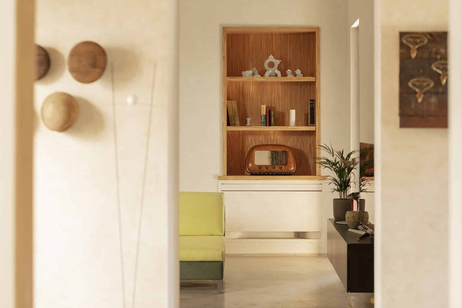 Modern interior design featuring a minimalist hallway leading to a stylish living area with a green chair, wooden shelving, decorative items, and a plant, creating a warm and inviting atmosphere. | Only on SopranoVillas