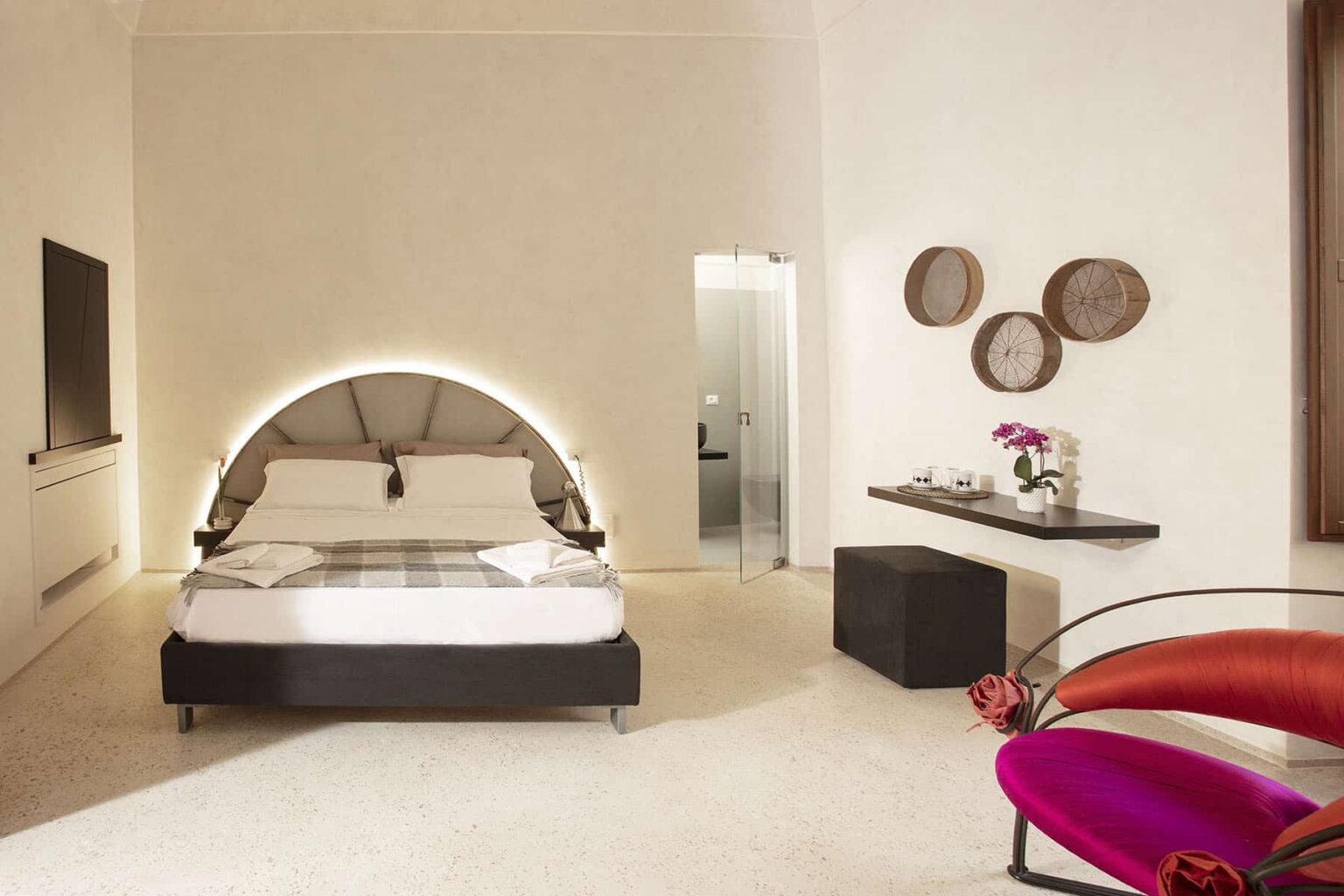 Modern hotel room featuring a stylish bed with ambient lighting, minimalist decor, a flat-screen TV, and a small seating area with decorative elements. Ideal for travelers seeking comfort and elegance. | Only on SopranoVillas