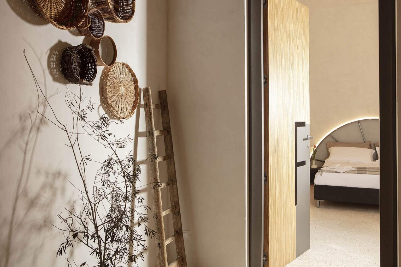 Interior view of a stylishly designed bedroom entrance featuring decorative woven baskets on the wall, a wooden ladder, and a minimalist aesthetic with natural elements. | Only on SopranoVillas