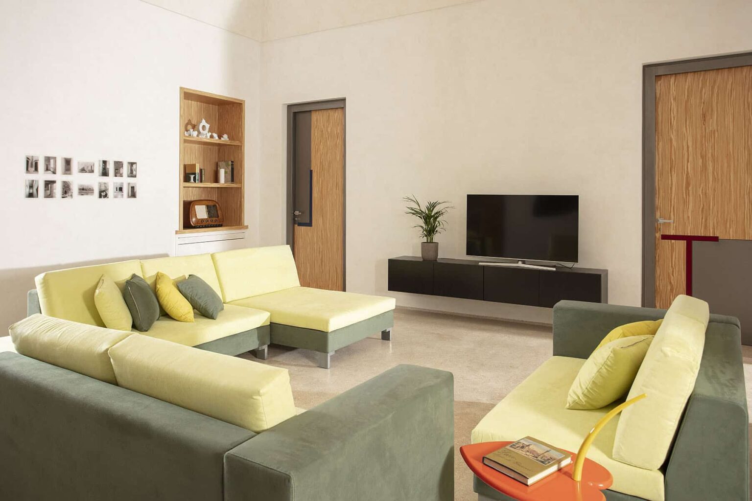 Modern living room featuring a comfortable sectional sofa in green and yellow, a sleek black TV stand, and a minimalist decor with a small plant. The walls are painted in neutral tones, enhancing the bright and airy atmosphere. | Only on SopranoVillas