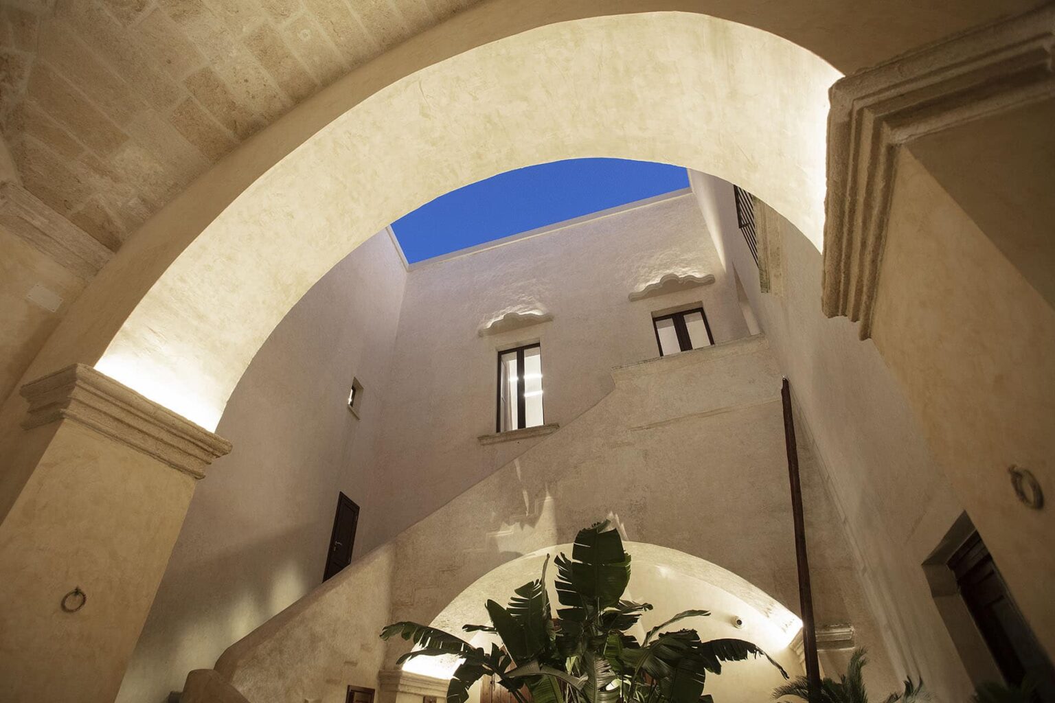 Interior view of a beautifully designed atrium featuring arched ceilings, natural light streaming in from above, and lush greenery at the base, showcasing a blend of modern and traditional architectural elements. | Only on SopranoVillas