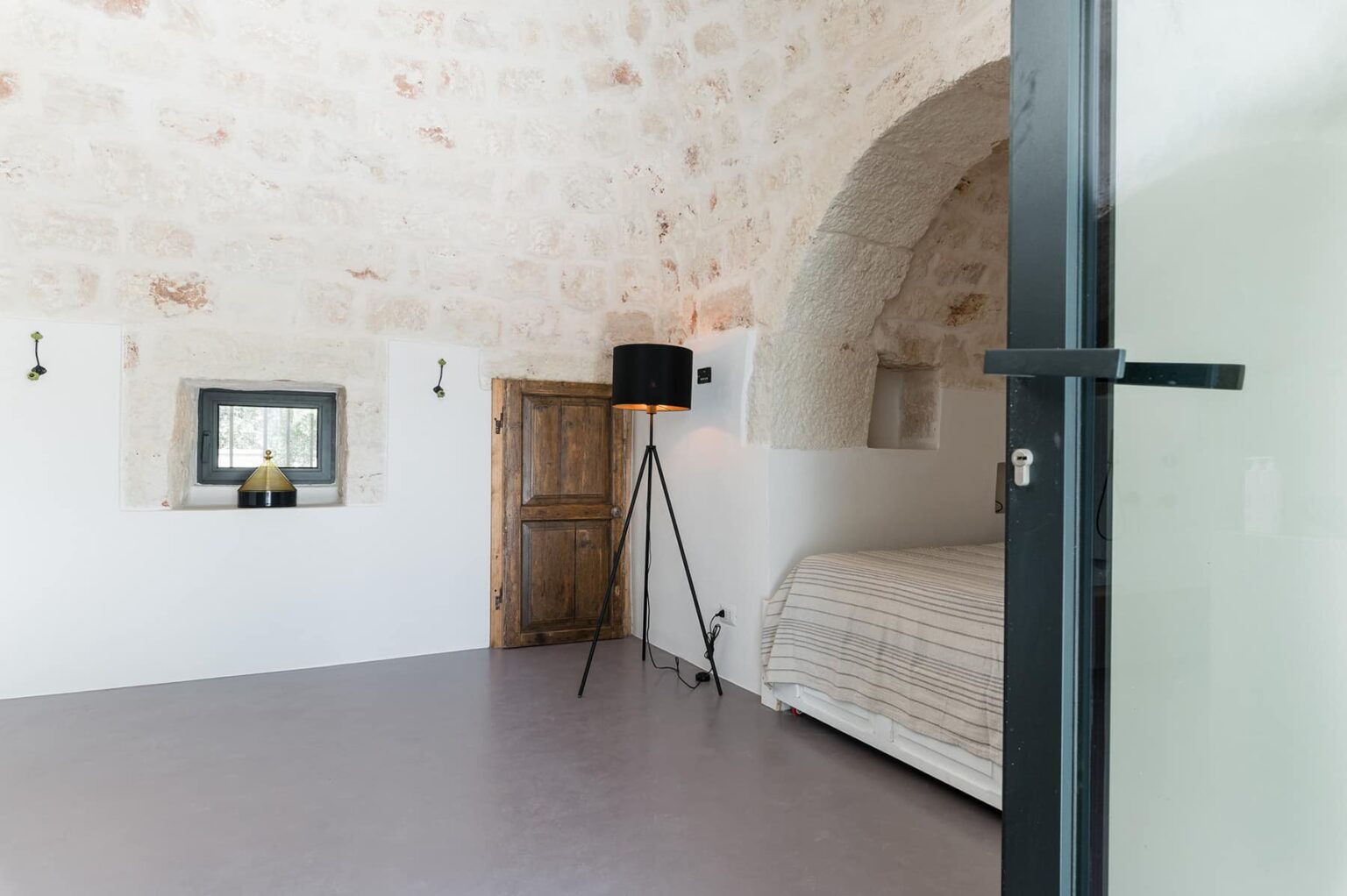 Modern minimalist bedroom featuring a stone arched ceiling, a cozy bed, wooden door, and stylish decor elements, creating a serene and inviting atmosphere. | Only on SopranoVillas