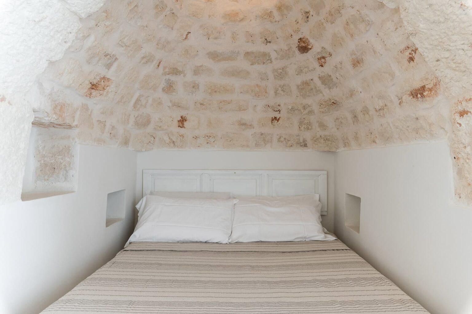 Cozy bedroom with a stone arched ceiling, featuring a neatly made bed with white pillows and a striped blanket, ideal for a relaxing stay. | Only on SopranoVillas