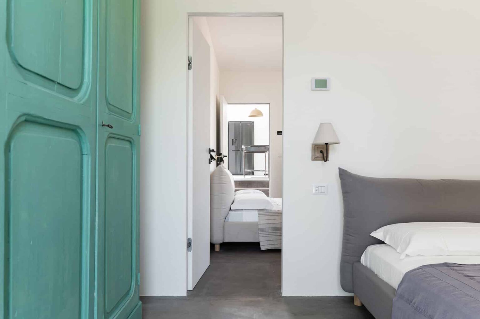 Modern bedroom interior featuring a green wardrobe, minimalist decor, and a view into a second room. The design emphasizes natural light and a neutral color palette, creating a serene atmosphere. | Only on SopranoVillas