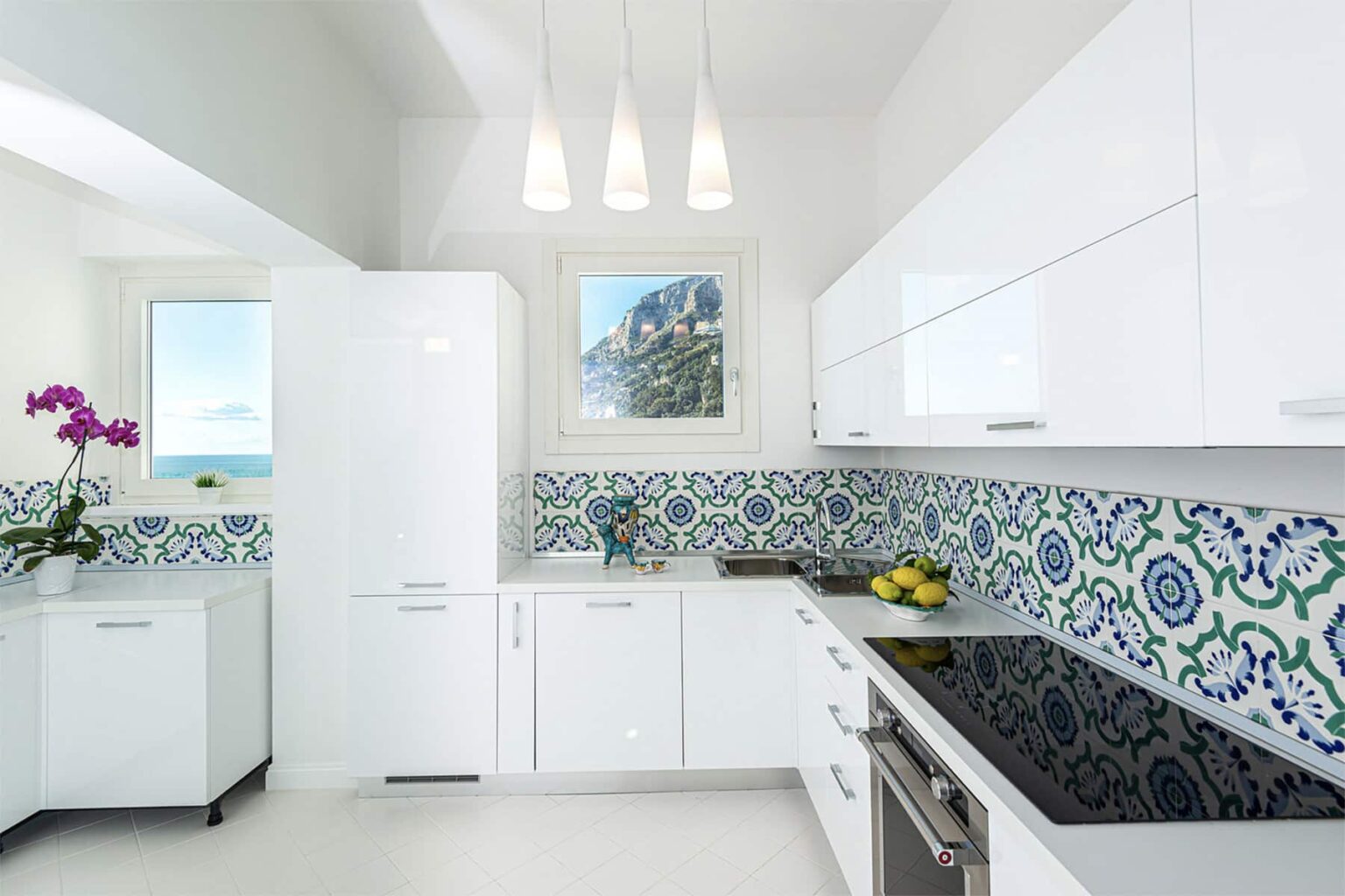 Modern kitchen with white cabinetry, colorful patterned backsplash, stainless steel appliances, and a bright window showcasing a scenic view. | Only on SopranoVillas