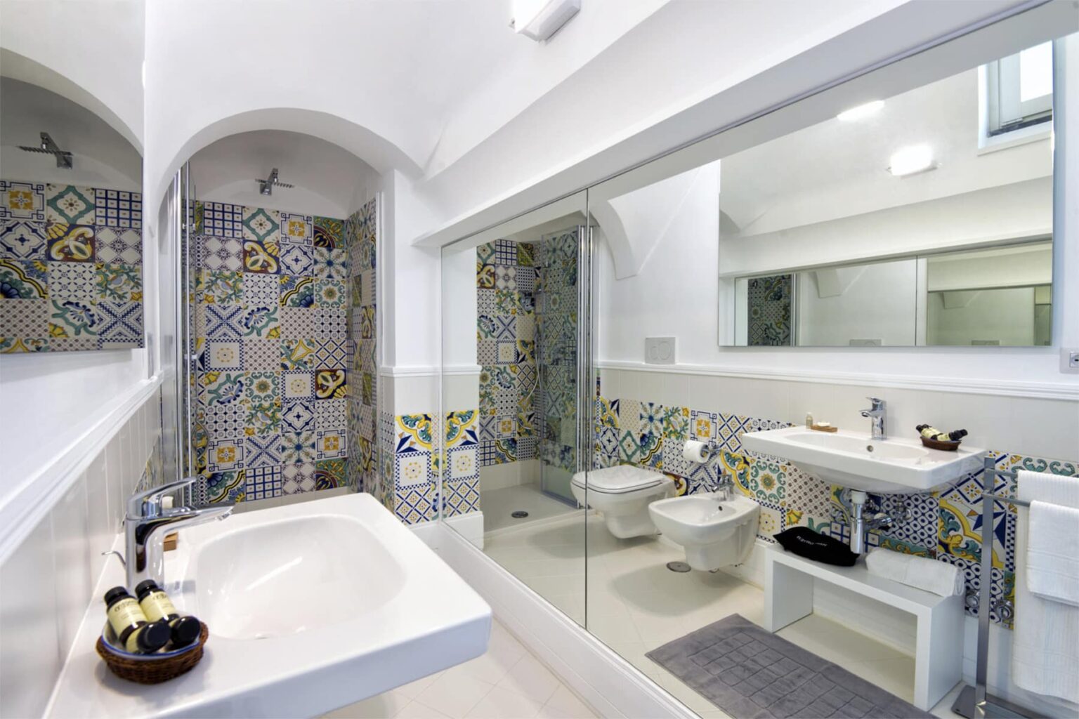 Modern bathroom featuring colorful patterned tiles, a spacious bathtub, a sleek sink, and a large mirror, creating a bright and inviting atmosphere. | Only on SopranoVillas