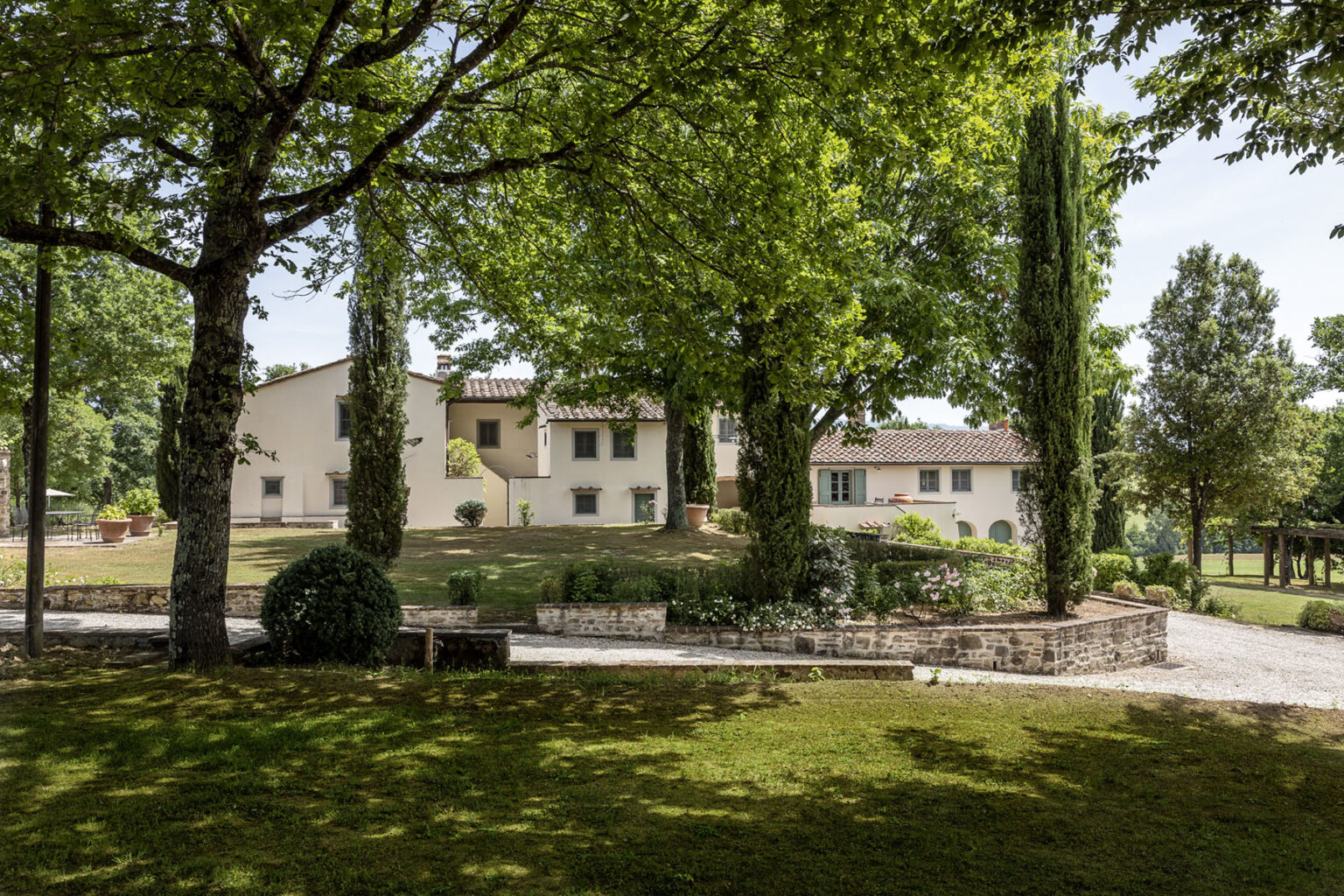 Scenic view of a charming villa surrounded by lush greenery and trees, featuring a well-maintained garden and pathways in a tranquil outdoor setting. | Only on SopranoVillas