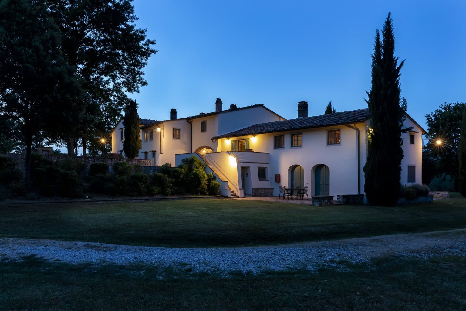 Charming countryside villa illuminated at dusk, featuring a spacious garden and elegant architecture surrounded by trees. | Only on SopranoVillas