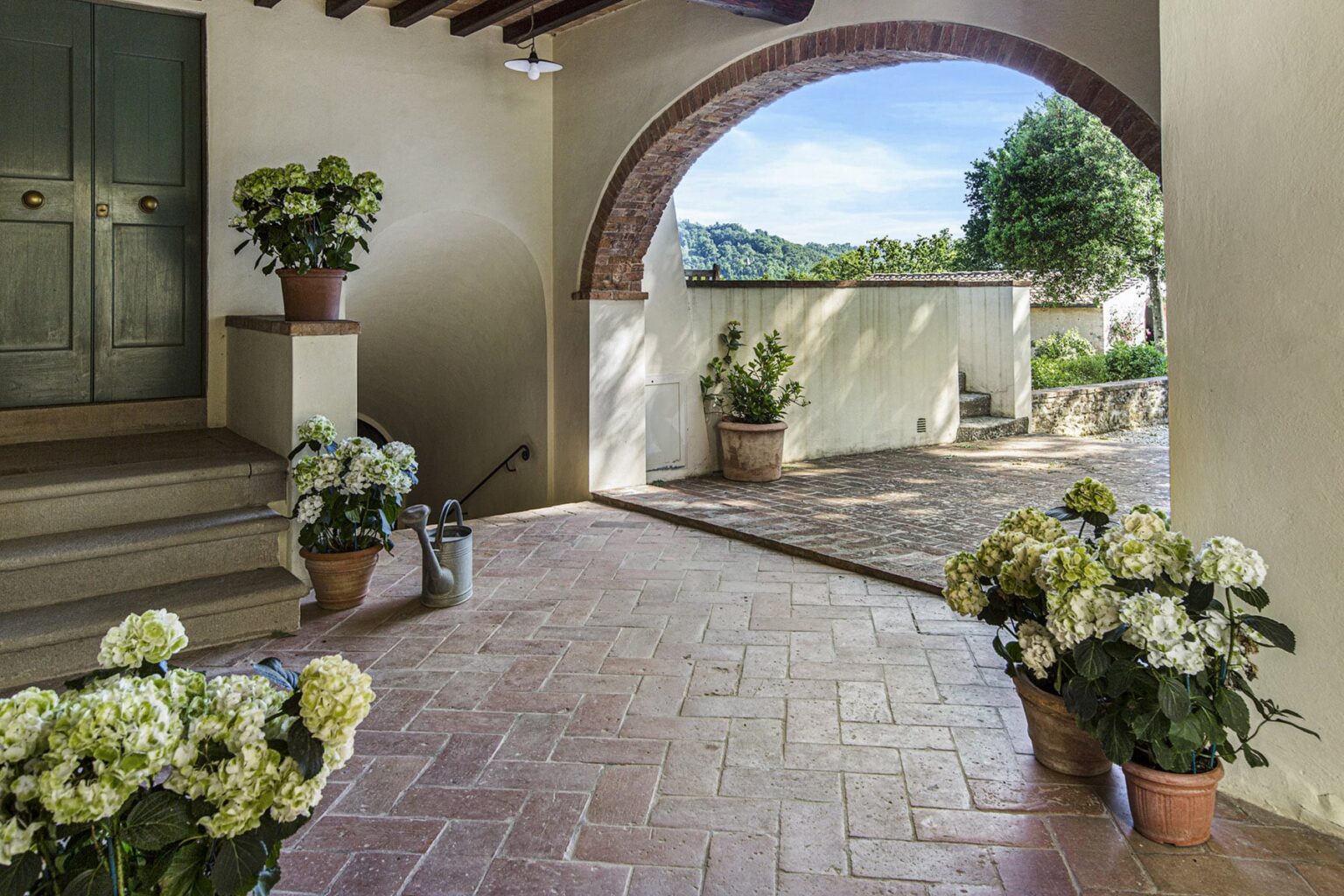 Welcoming entrance with arched doorway, featuring potted hydrangeas and a tiled floor, leading to a scenic outdoor area with greenery. | Only on SopranoVillas