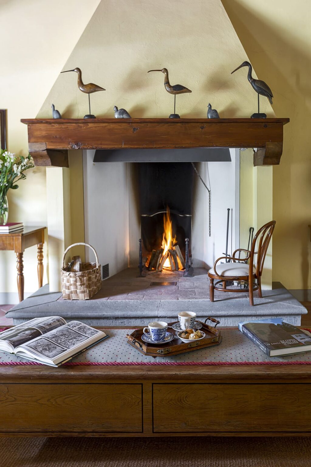 Cozy living room featuring a traditional stone fireplace with a roaring fire, a woven basket, and a wooden chair, creating a warm and inviting atmosphere. | Only on SopranoVillas