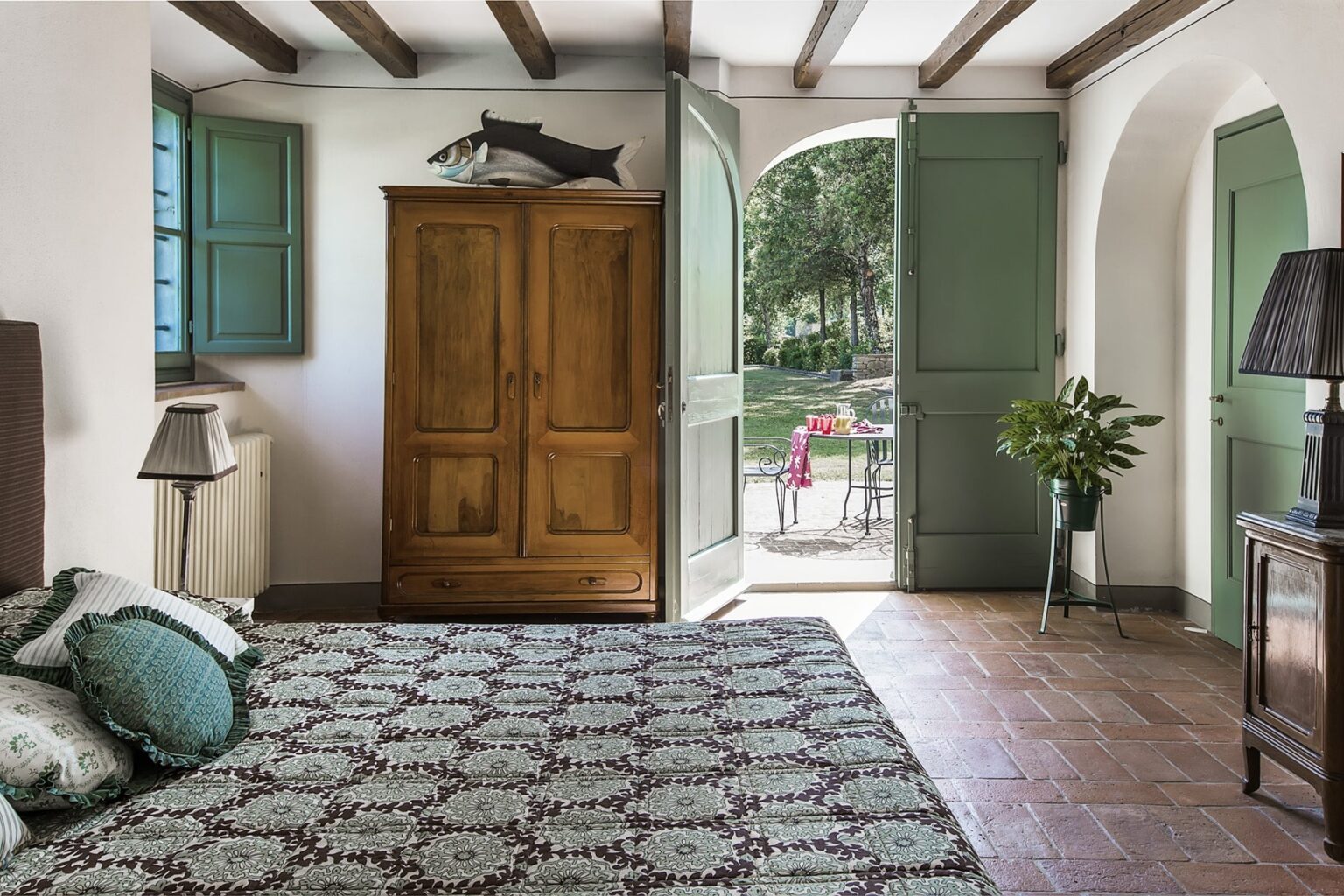 Spacious bedroom featuring a wooden wardrobe, patterned rug, and natural light from open doors leading to a garden view. | Only on SopranoVillas