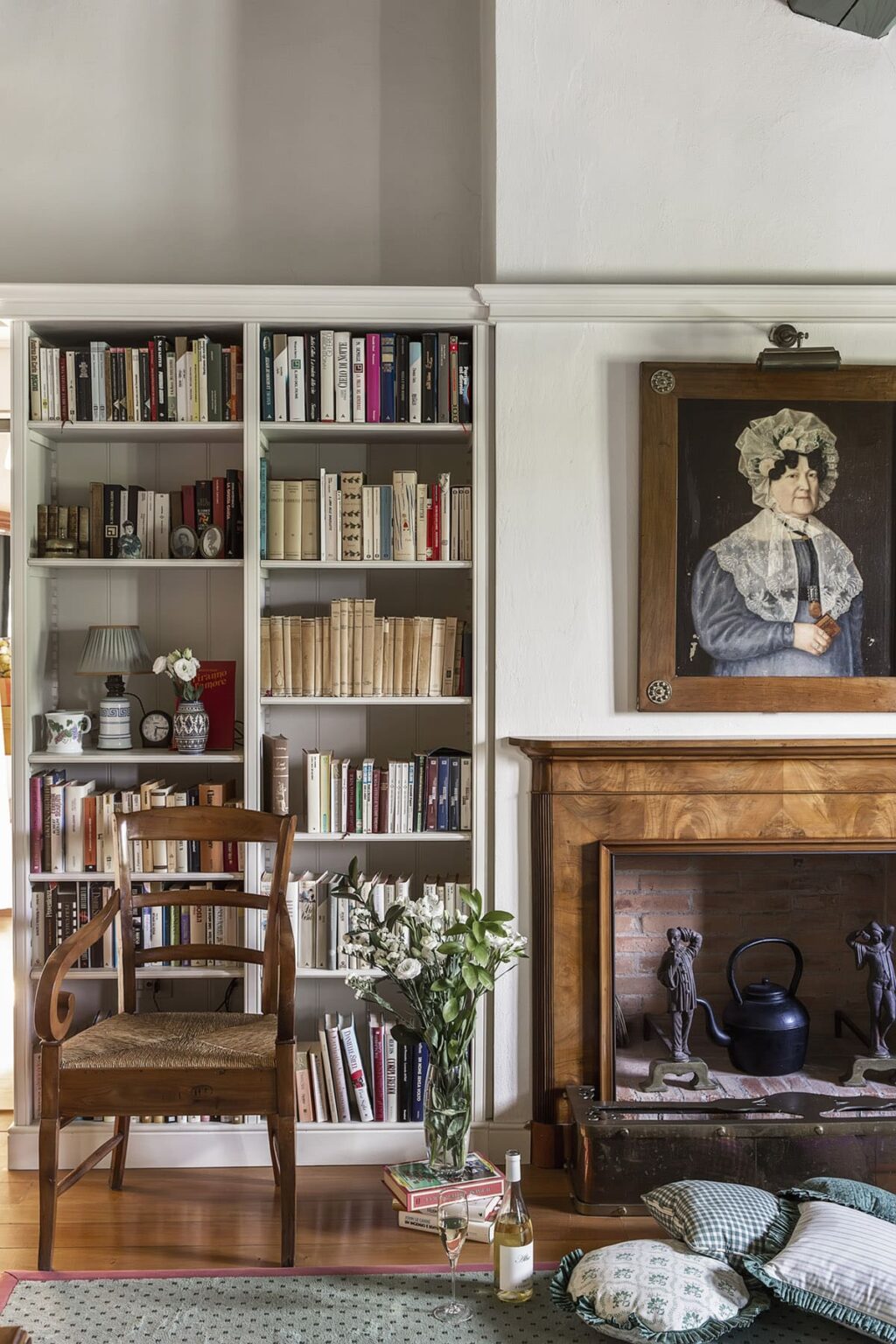 Cozy reading nook featuring a wooden chair, a well-stocked bookshelf filled with various books, and a vintage portrait hanging above a classic fireplace, creating a warm and inviting atmosphere. | Only on SopranoVillas