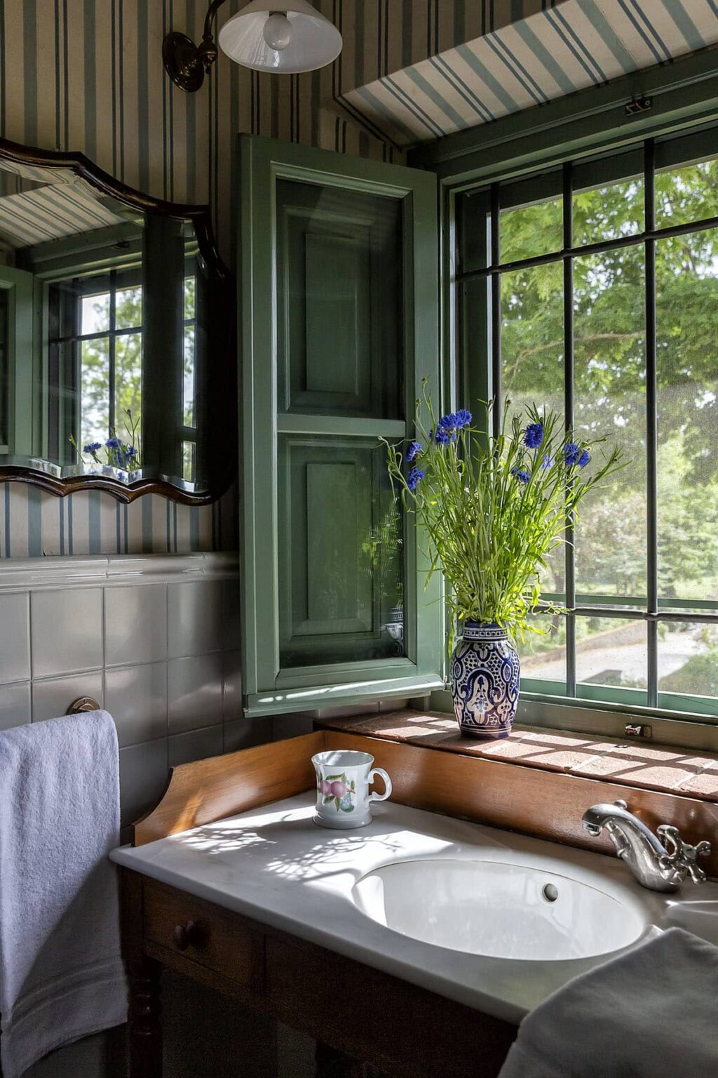 A bright interior featuring green shutters and a large window, with a vase of blue flowers on a wooden table, creating a serene and inviting atmosphere. | Only on SopranoVillas