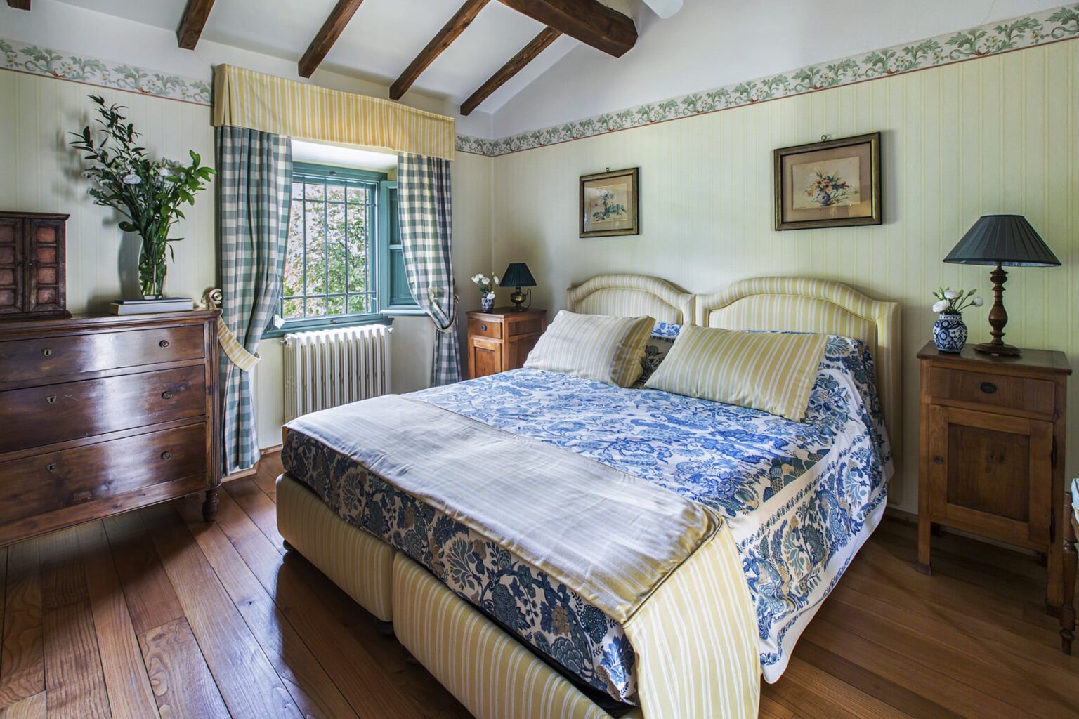 Cozy bedroom featuring a queen-sized bed with decorative bedding, wooden furniture, and vintage decor. Natural light streams through a green window, enhancing the inviting atmosphere. | Only on SopranoVillas