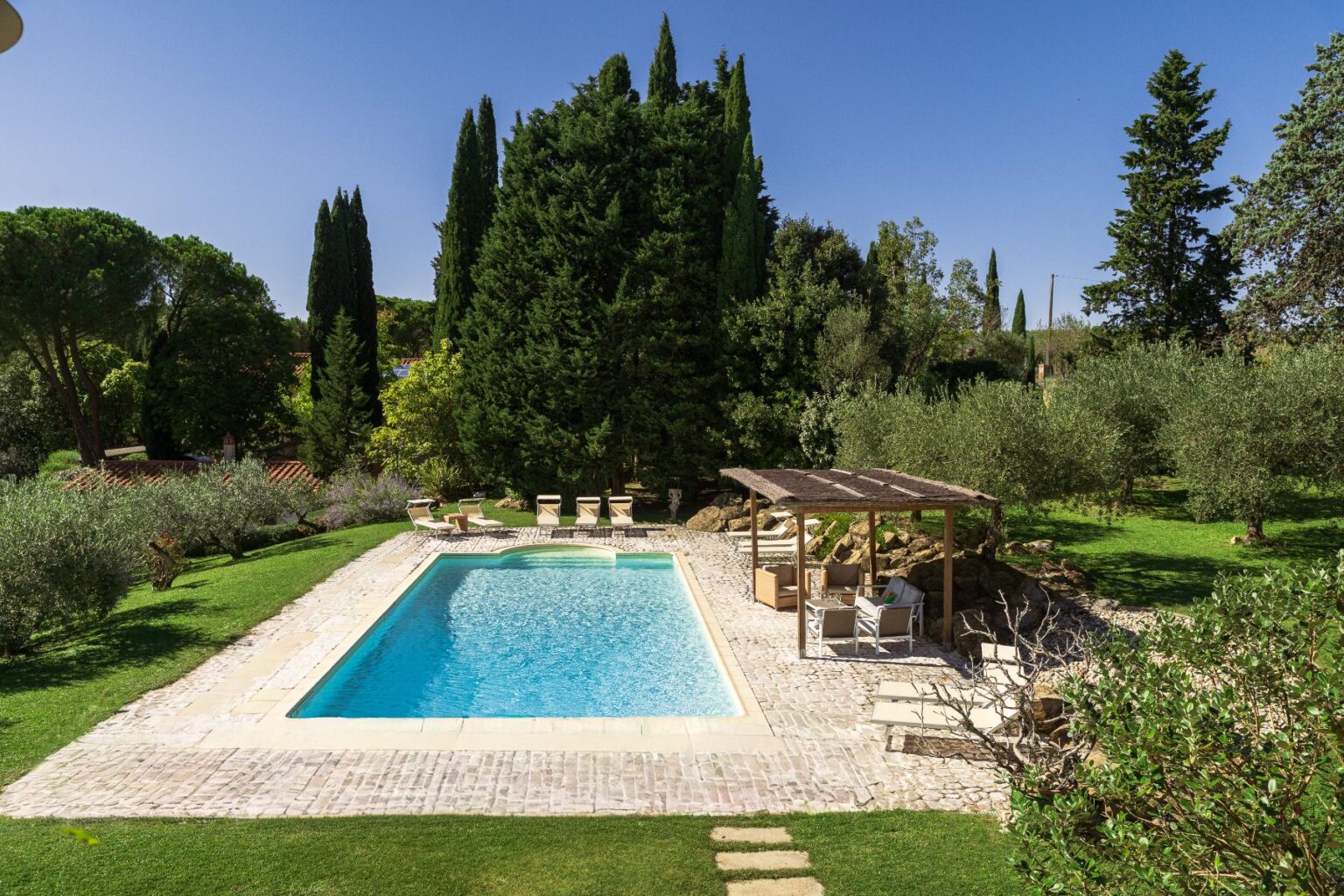 Beautiful outdoor swimming pool surrounded by lush greenery, comfortable lounge chairs, and a shaded seating area, perfect for relaxation and enjoyment in a serene garden setting. | Only on SopranoVillas