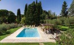Beautiful outdoor swimming pool surrounded by lush greenery, comfortable lounge chairs, and a shaded seating area, perfect for relaxation and enjoyment in a serene garden setting.