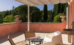 Spacious terrace with stylish outdoor furniture, including a black table and woven chairs, overlooking lush greenery and decorative planters under a canopy. Ideal for relaxation and enjoying scenic views.
