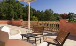 Spacious outdoor terrace featuring modern white seating, a black table with wine glasses, and a scenic view of lush greenery and decorative planters, perfect for relaxation and entertaining.