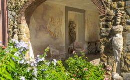 Charming outdoor patio featuring stone walls, decorative sculptures, and elegant seating surrounded by colorful flowers, showcasing artistic murals on the walls for a serene garden atmosphere.