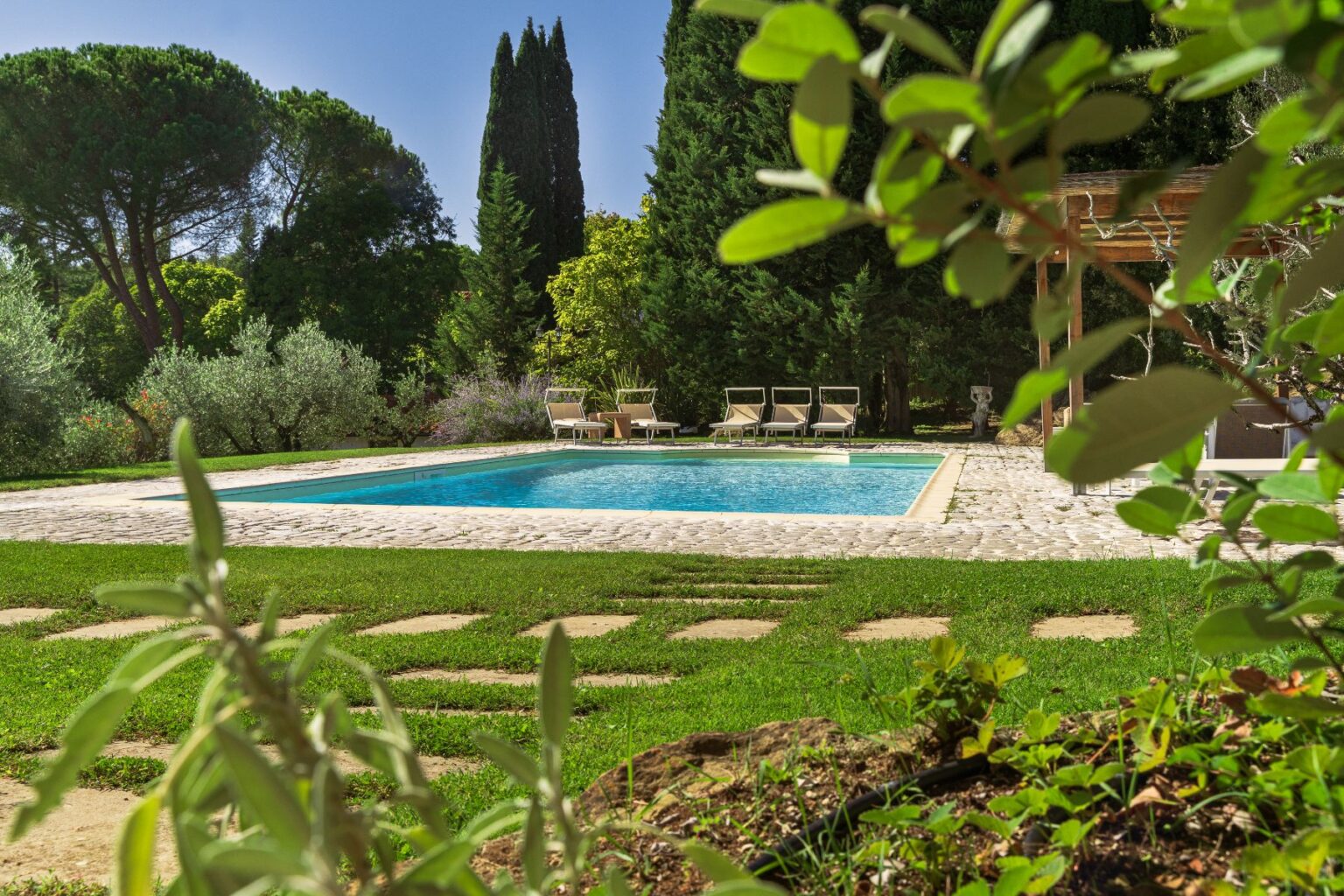 Serene backyard oasis featuring a crystal-clear swimming pool surrounded by lush greenery, stone pathways, and comfortable lounge chairs, ideal for relaxation and outdoor gatherings. | Only on SopranoVillas