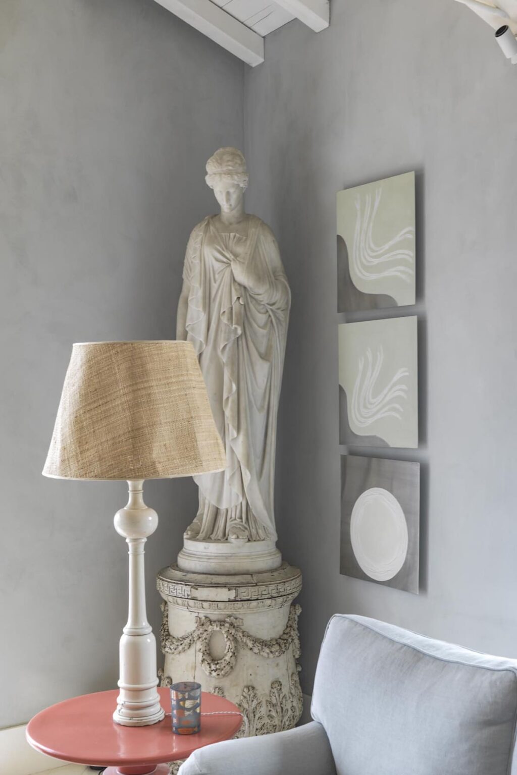Interior decor featuring a marble statue, a textured lamp with a beige shade, and three minimalist abstract paintings on a gray wall, creating a serene and stylish atmosphere. | Only on SopranoVillas