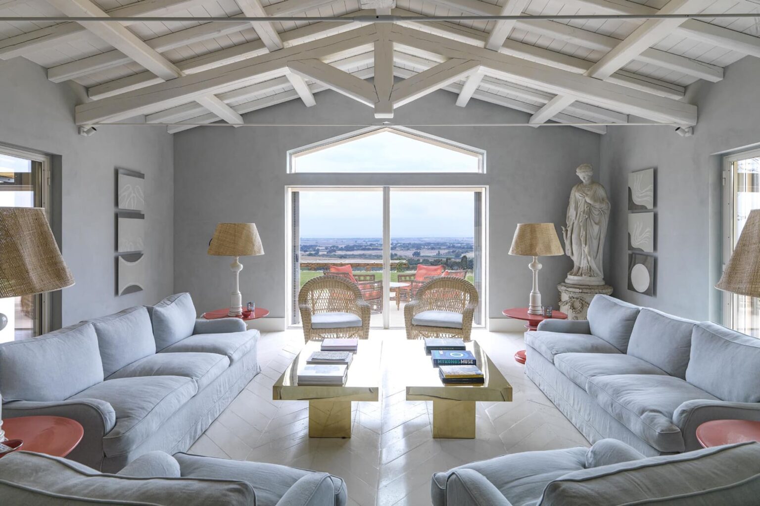 Spacious modern living room with white sofas, a gold coffee table, and large windows offering a scenic view, complemented by stylish lamps and a statue. | Only on SopranoVillas