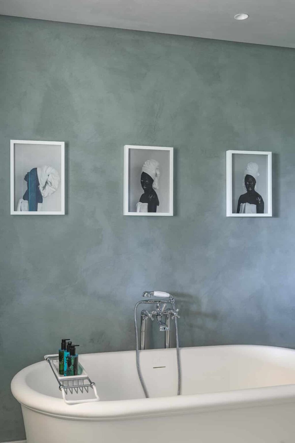 Three framed black-and-white portraits of individuals with head coverings displayed on a textured green wall, showcasing a modern art aesthetic. A glass table is positioned in front, enhancing the contemporary interior design. | Only on SopranoVillas