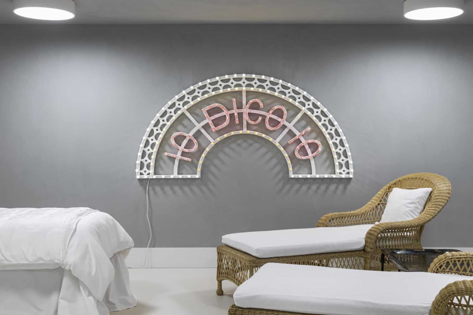Modern spa interior featuring a decorative neon sign with a rainbow design in pink and white, complemented by stylish wicker lounge chairs and soft lighting. | Only on SopranoVillas