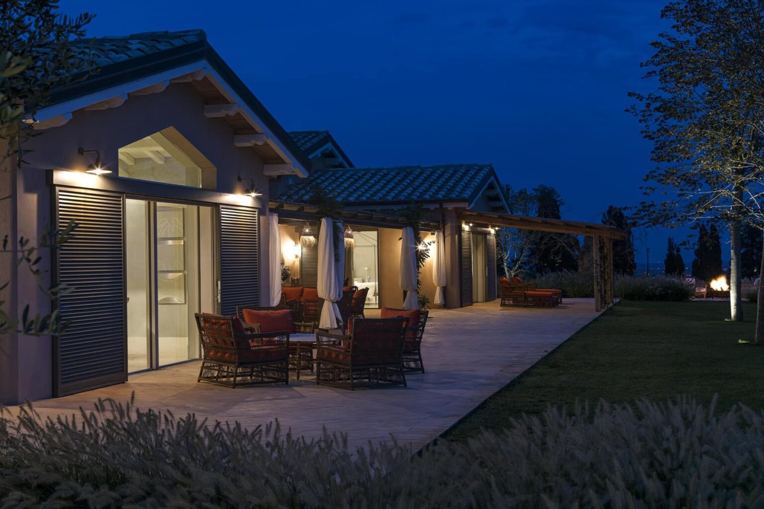 Modern outdoor patio at dusk featuring stylish furniture and soft lighting, surrounded by landscaped greenery. Ideal for evening gatherings and relaxation. | Only on SopranoVillas