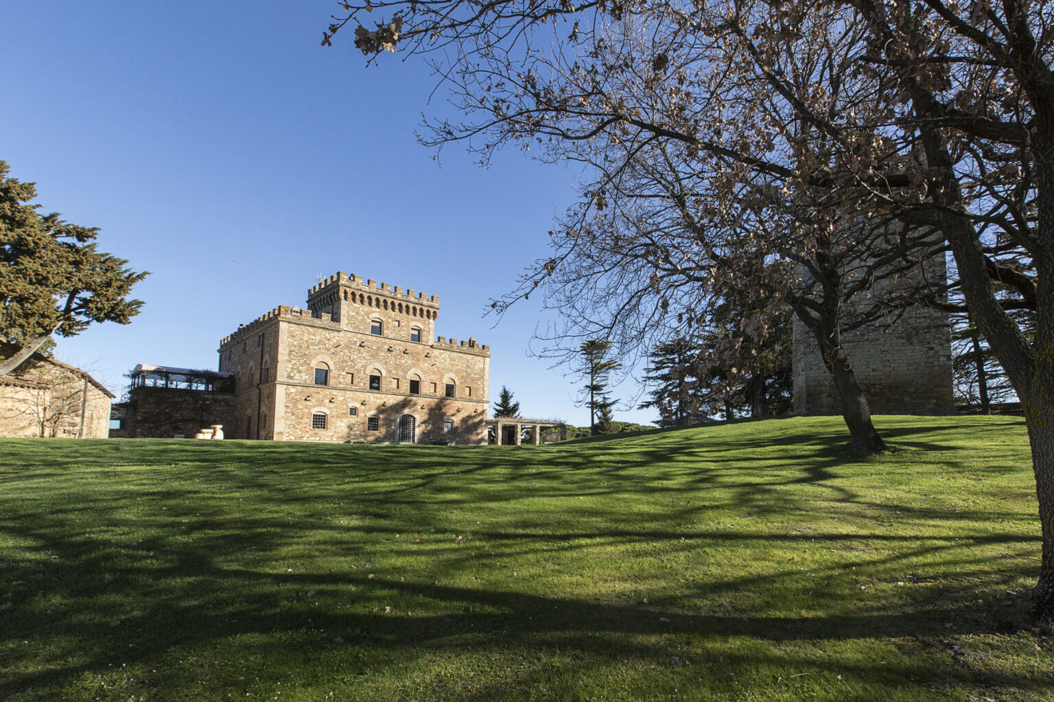 Historic stone castle on a grassy hillside, surrounded by trees under a clear blue sky. | Only on SopranoVillas