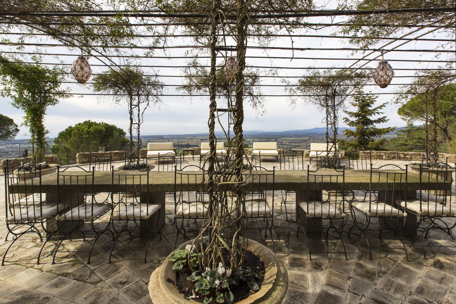 Outdoor dining area with metal chairs and tables under a trellis, featuring scenic views of rolling hills and trees. Ideal for gatherings and events in a tranquil setting. | Only on SopranoVillas