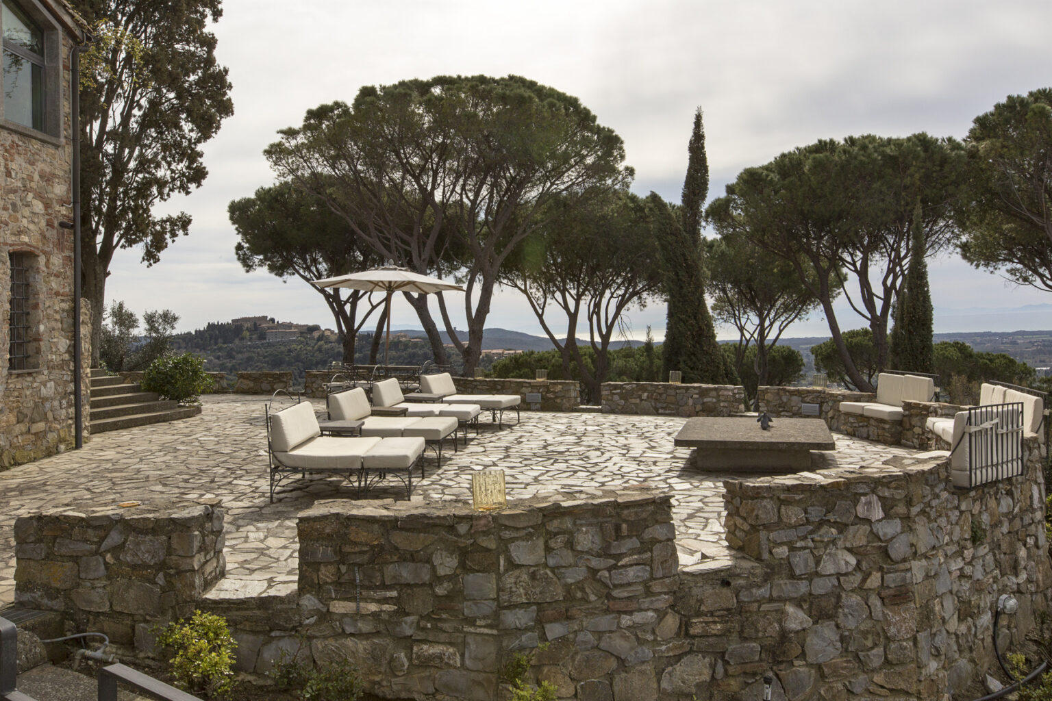 Outdoor patio area with stone walls, lounge chairs, and trees, offering scenic views of the landscape and sky. Ideal for relaxation and outdoor gatherings. | Only on SopranoVillas