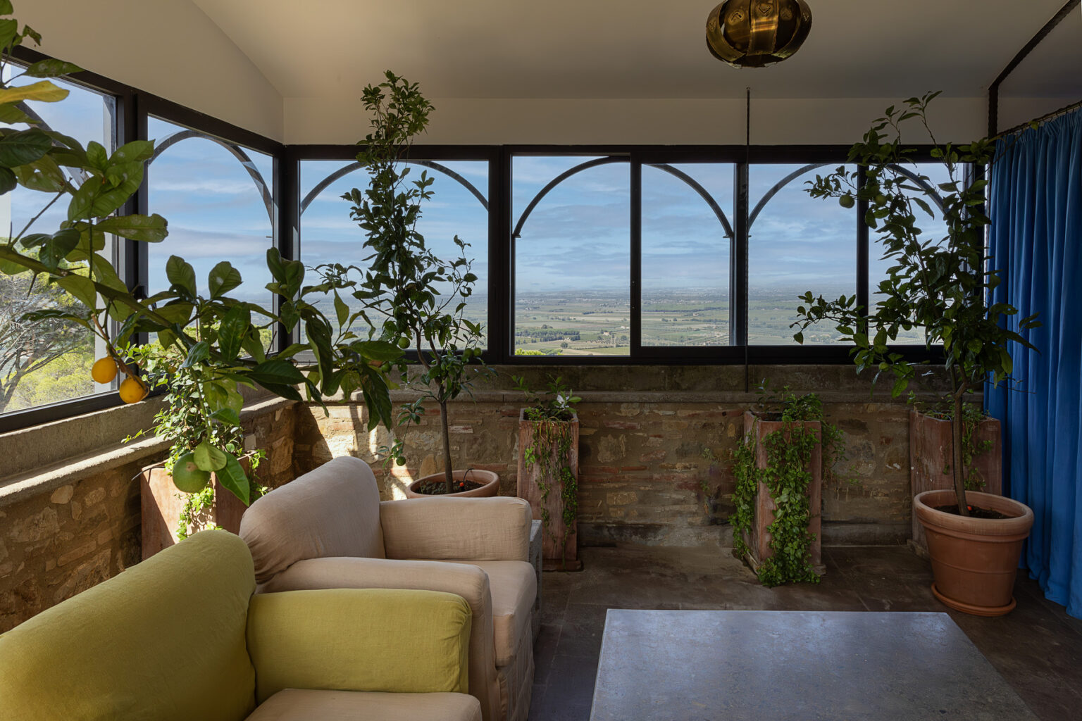 Cozy sunroom with large windows offering a scenic view, featuring green plants and comfortable seating. The space combines natural light with a relaxing atmosphere, ideal for enjoying nature indoors. | Only on SopranoVillas