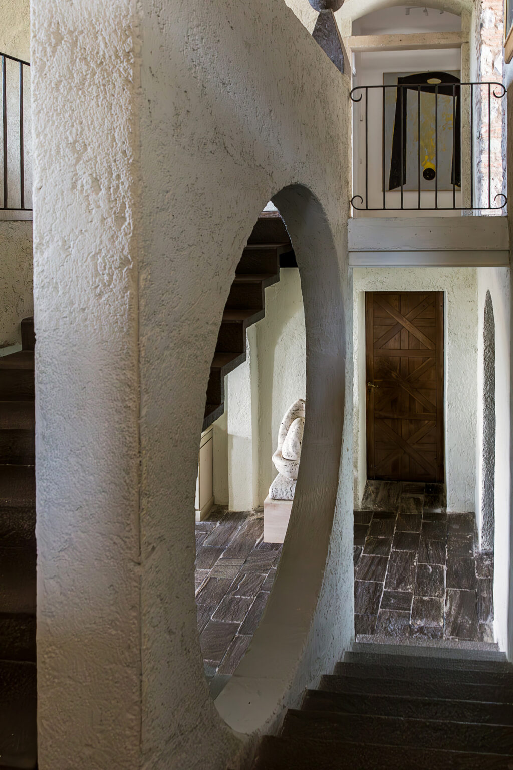 Interior view of a modern architectural space featuring a curved archway, wooden staircase, and a rustic wooden door, highlighting contemporary design elements and textures. | Only on SopranoVillas
