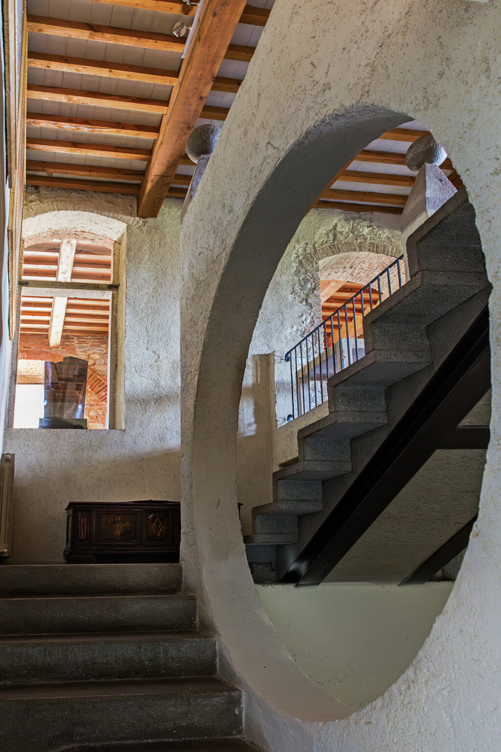 Interior view of a rustic staircase leading to a second floor, featuring textured walls and natural light streaming through large windows. The design includes a mix of modern and traditional elements, creating a warm and inviting atmosphere. | Only on SopranoVillas