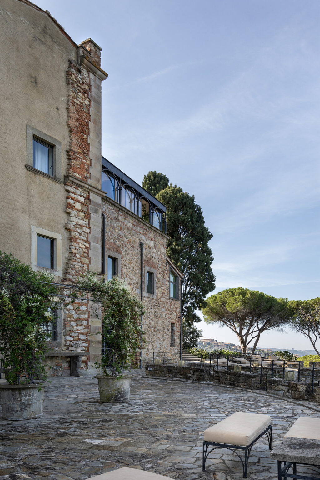Historic stone building with modern windows, surrounded by greenery and a tall tree, under a clear blue sky. | Only on SopranoVillas
