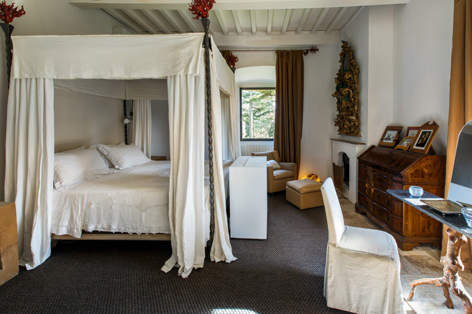 Cozy bedroom featuring a four-poster bed with white drapes, elegant wooden furniture, a desk, and a warm color palette, illuminated by natural light from a window. | Only on SopranoVillas